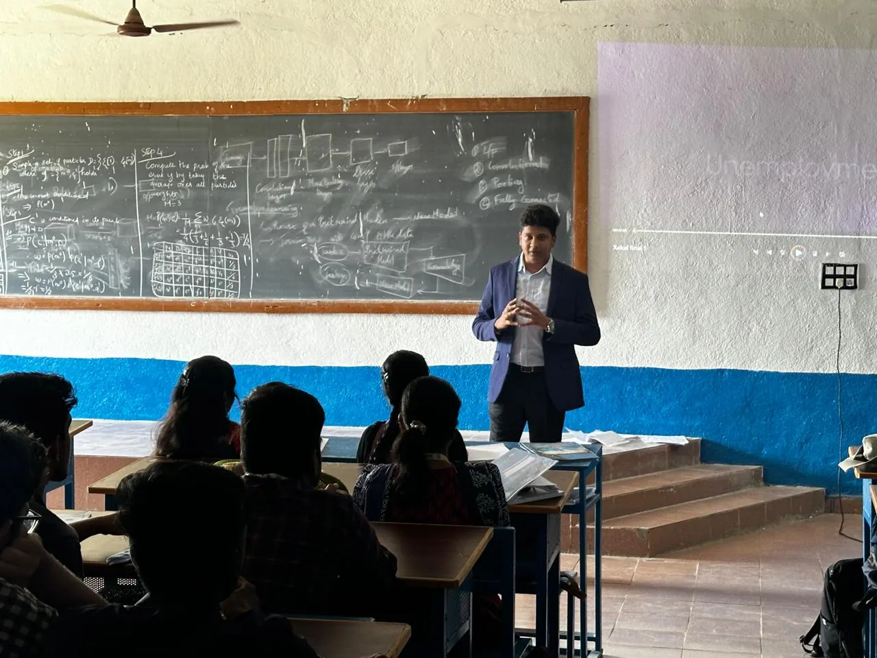 A Xakal speaker talks to students in front of a chalkboard